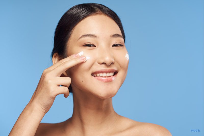 Woman applying skin care products on a blue background.