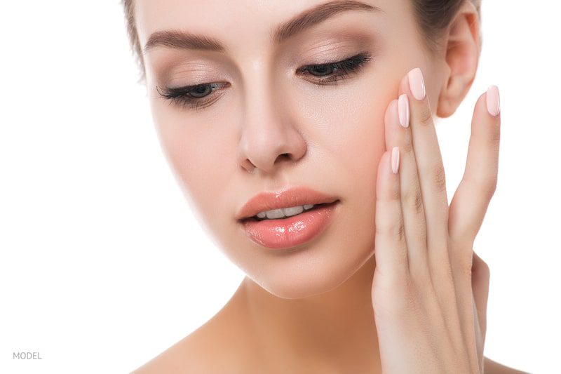 Young woman touching her smooth cheek with her fingers. 