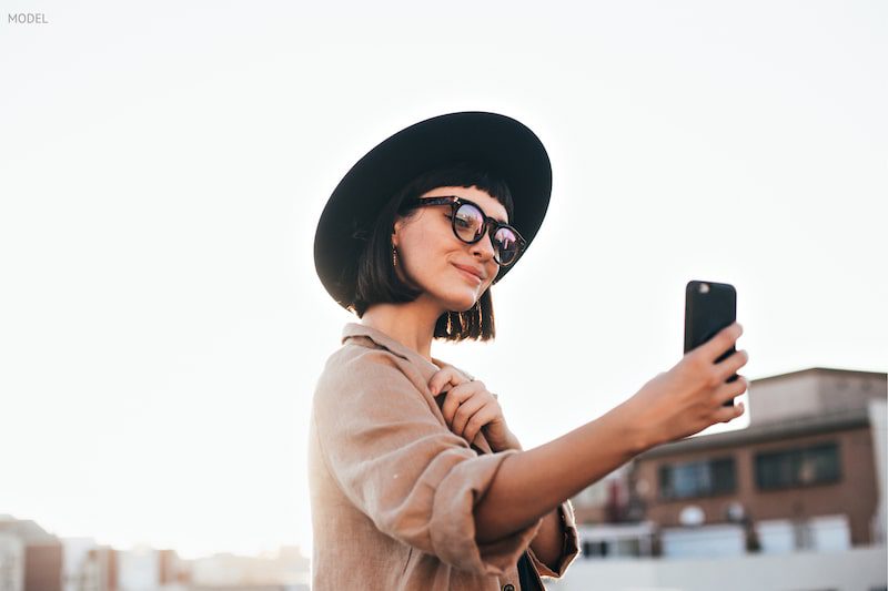 Woman in a black hat and glasses taking a selfie on rooftop