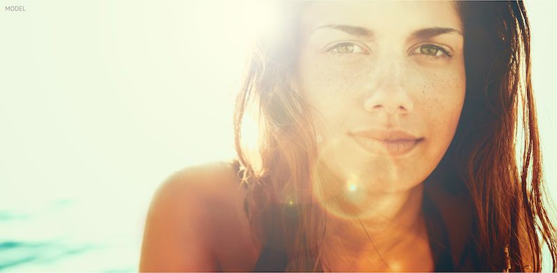 Woman with sun rays shining across her face while at the beach