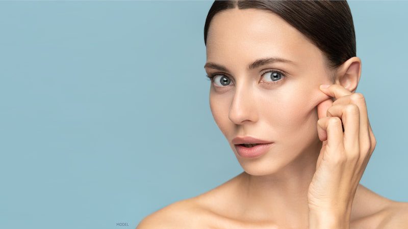 Woman grabbing her cheek skin against a blue background.