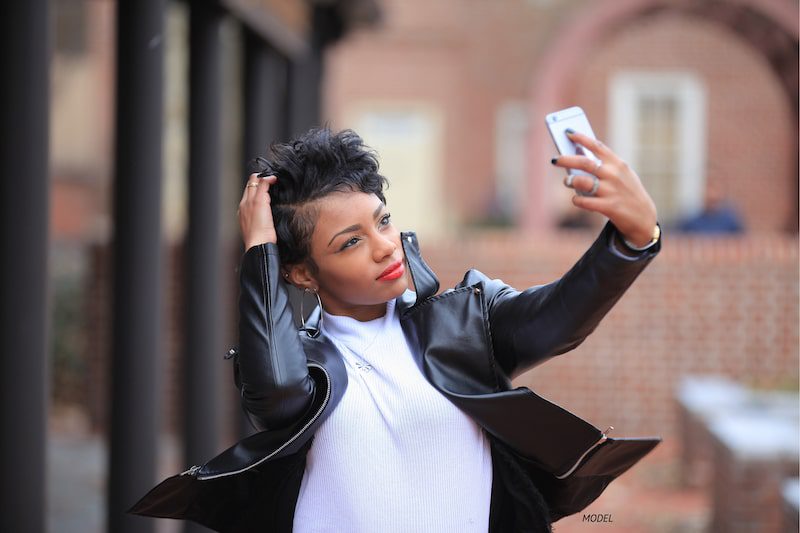 Young woman taking selfie in front of brick building.